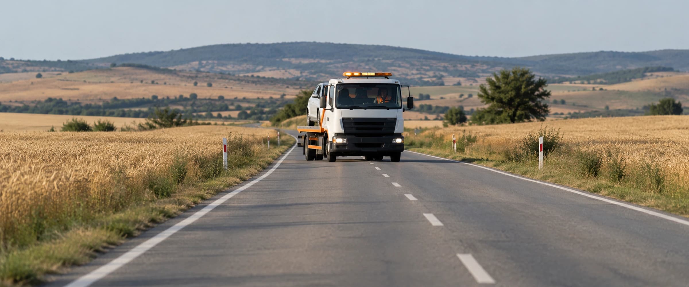 Buğday tarlaları arasından geçen iki şeritli kırsal yol, uzakta bir çekici (bölge tipini temsil eden görsel)